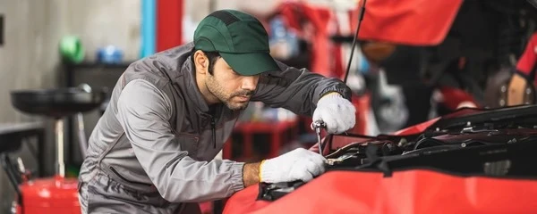 Mécanicien automobile souriant en combinaison bleue et casquette travaillant sous le capot ouvert d'un véhicule dans un garage